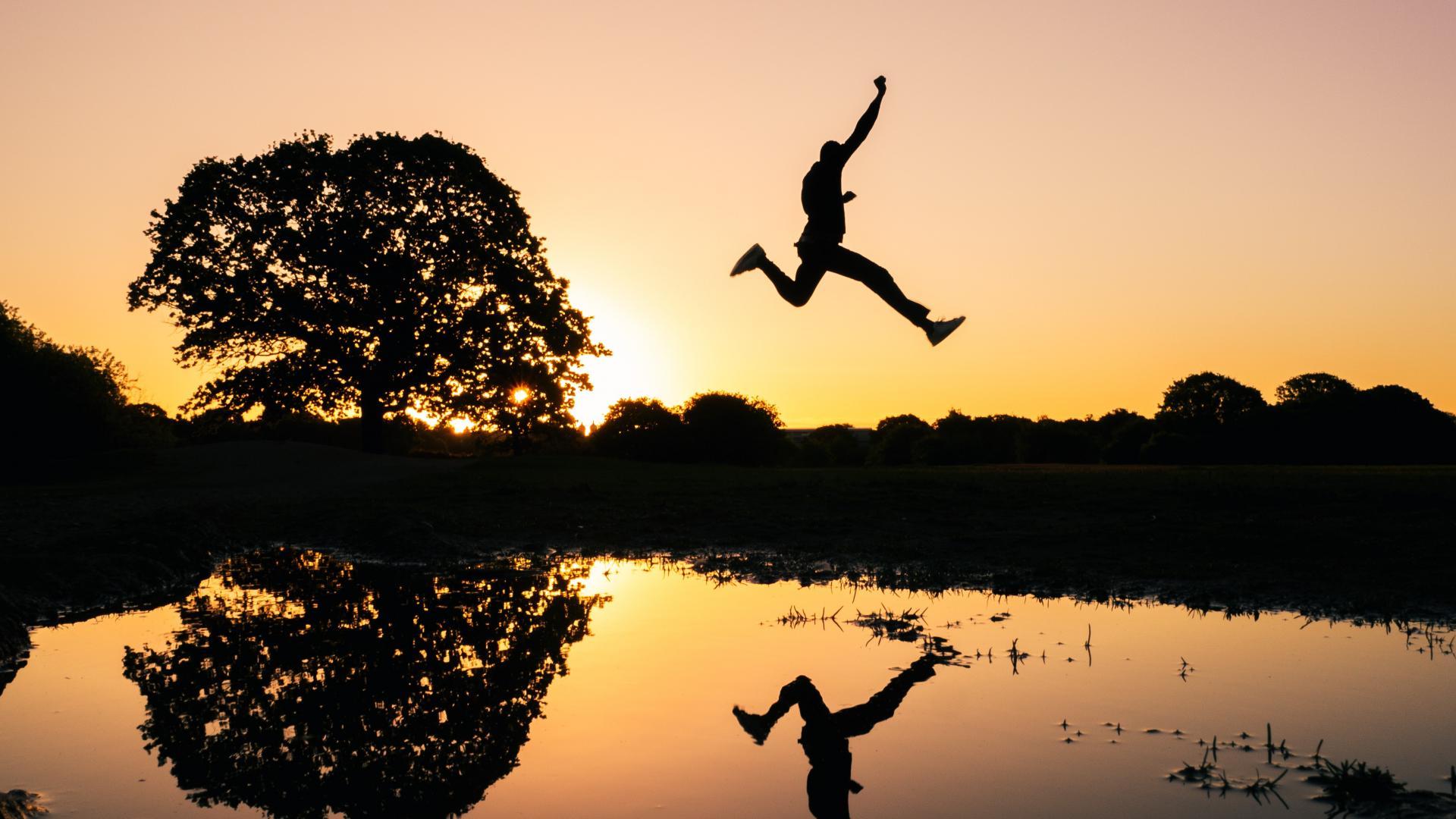 Homme qui saute au-dessus d'un lac sous un coucher de soleil